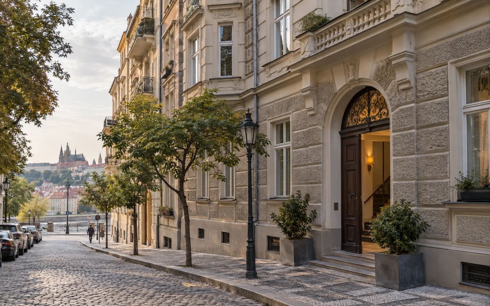 A cobbled Prague street of historic apartment façades with an open entrance doorway.